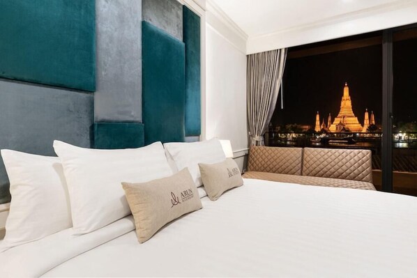 A hotel room with a bed, pillows, and a view of a temple at night. - Arun Riverside Bangkok (Bangkok)