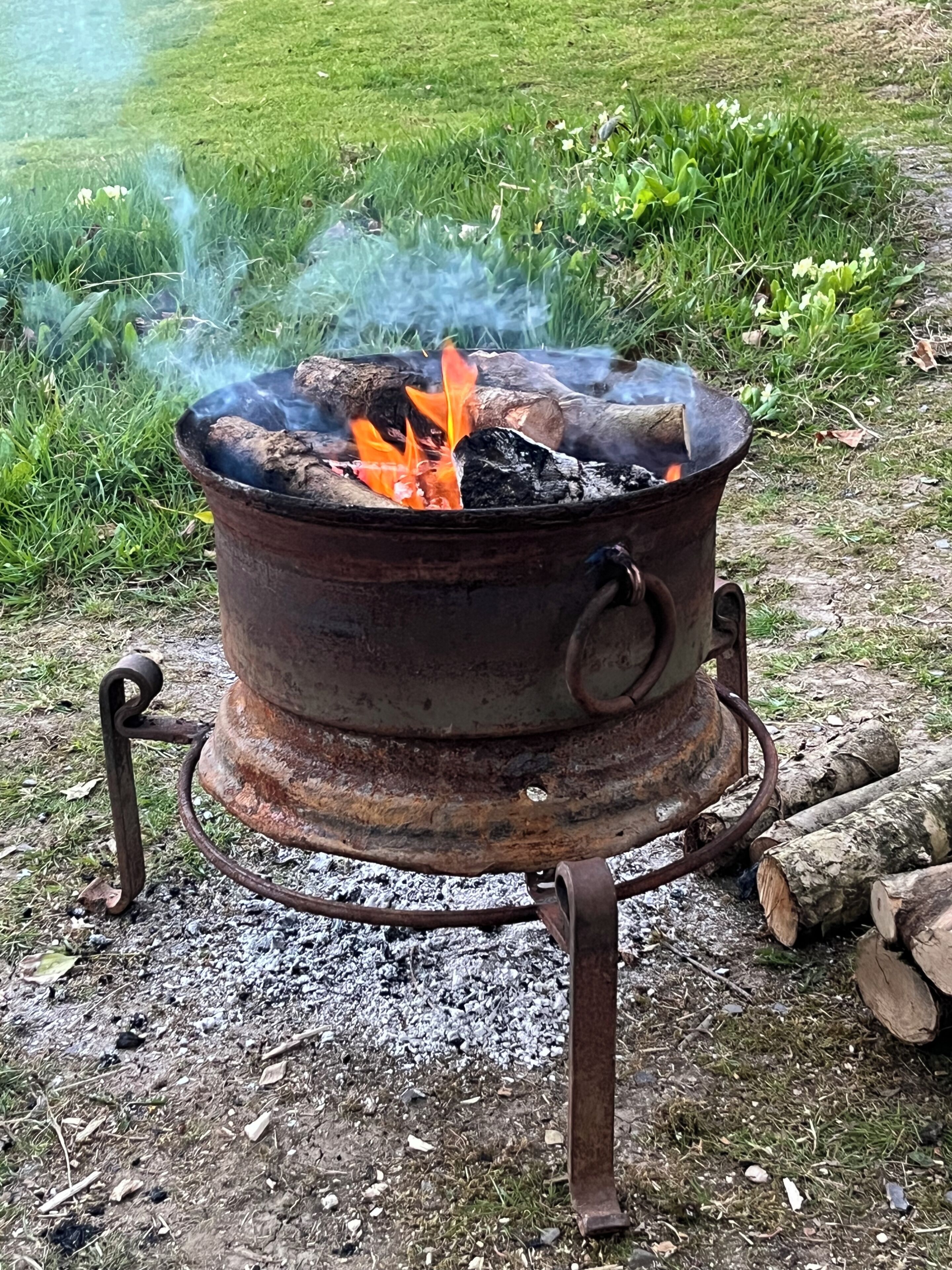 Un réchaud de cuisson portatif pour l’extérieur, avec un feu allumé à l’intérieur, entouré de bûches et de gravier.