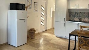A compact kitchen with white cabinets, a microwave, and a refrigerator. There is a dining area with a wooden table and chairs.