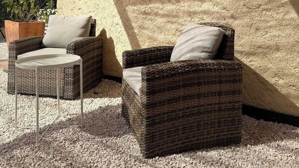 A covered outdoor seating area with wicker furniture and a textured wall.