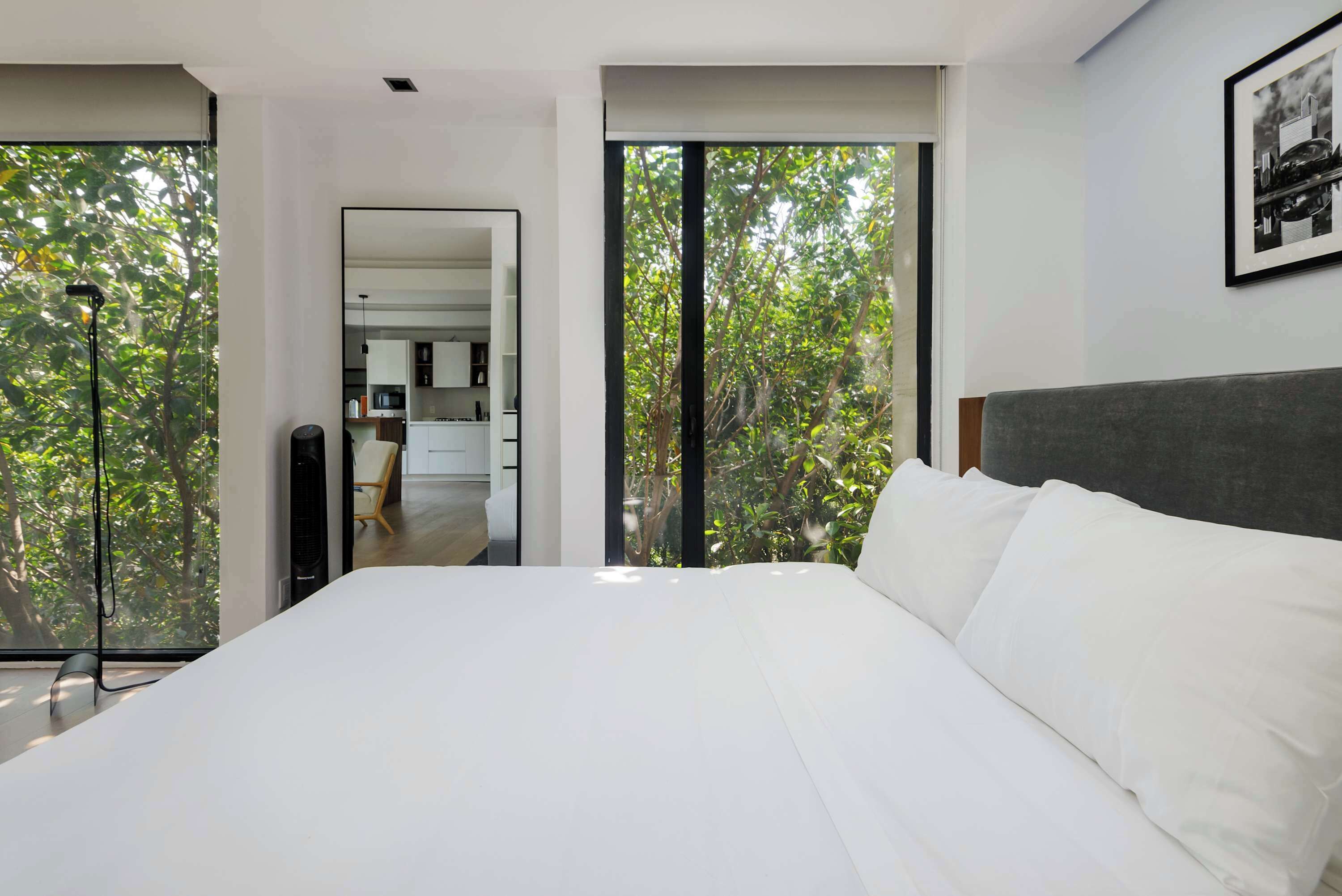 A modern bedroom with a large bed, a view of the outdoors through floor-to-ceiling windows, and a minimalist design.