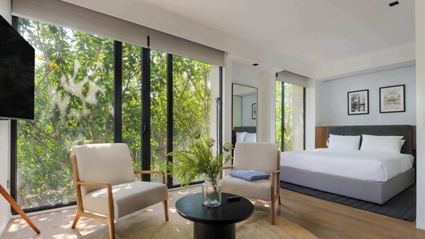 A modern bedroom with a large bed, two armchairs, a coffee table, and a TV. - Breathtaking loft in Roma Norte (Ciudad de México)