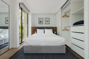A modern hotel room with a large bed, a walk-in closet, and a view of greenery through the window. - Breathtaking loft in Roma Norte (Ciudad de México)