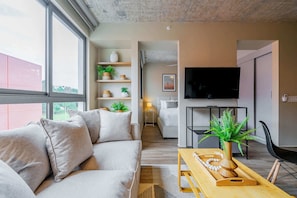 A modern living room with a sofa, a wooden coffee table, and a TV. There is a staircase leading to another room. - w* | Cozy 1BR in Panama Pacifico w/ Pool (Panamá)