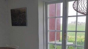 A room with a dining table and chairs, a large window with a view of a barn and green lawn, and a ceiling fan.