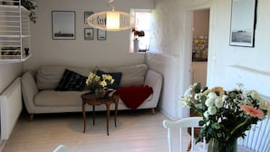 A living room with a sofa, a small table with a vase of flowers, a hanging light fixture, and a white chair.