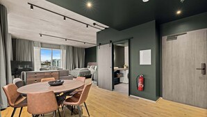 Una habitación de hotel moderna con zona de comedor, cama, televisor y extintor.