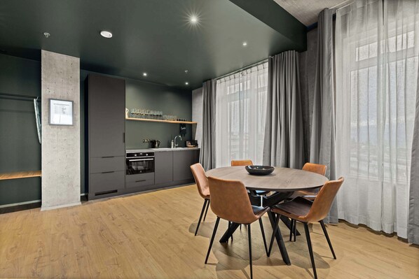 Una cocina moderna con armarios oscuros, una mesa redonda con sillas y un amplio ventanal con cortinas traslúcidas.
