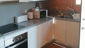 Una cocina compacta con armarios blancos, microondas, tostadora y fregadero.
