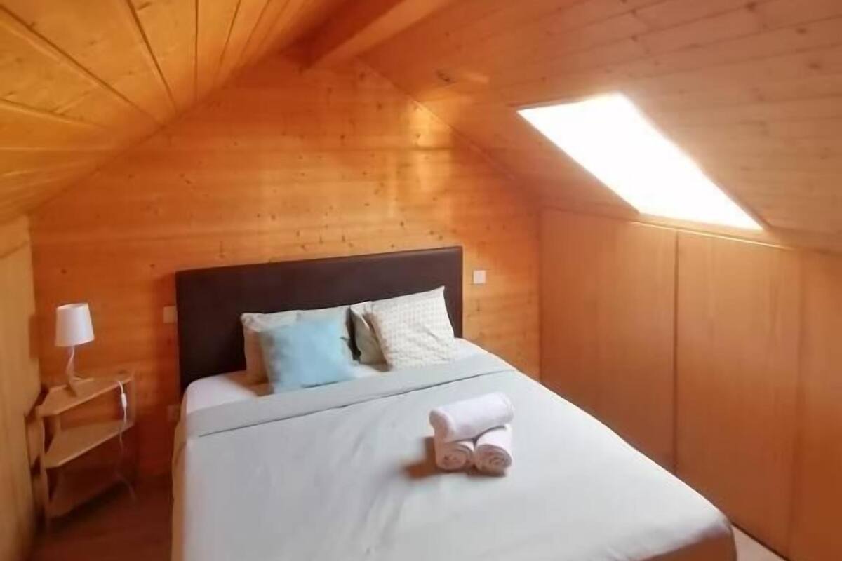 Une pièce chaleureuse en bois, avec un lit, une table de chevet et une lucarne.