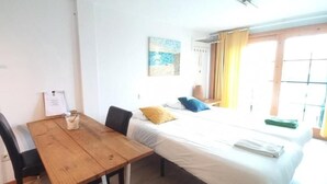 Una habitación con una mesa de madera, dos sillas, una cama con ropa blanca, un almohámero amarillo y un almohámero azul.