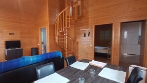 Una cabaña de madera con una mesa de comedor, sillas, un sofá, un televisor y una escalera.