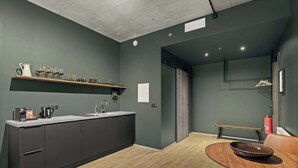 A modern kitchen with dark cabinets, a wooden countertop, and a dining area with a round table and a bowl. - Aurora Nooks - Superior Studio for 2 - free parking (Kópavogur)