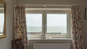 Ein Zimmer mit Meerblick durch ein Fenster mit blumigen Vorhängen.