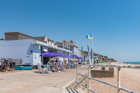 A beachside restaurant with outdoor seating, a flag, and a row of parked bicycles.