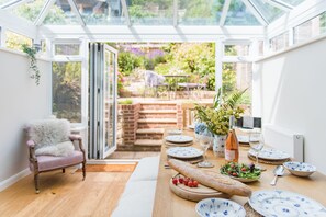 A conservatory with a dining table set for six, surrounded by white walls and a wooden floor.