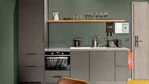 Eine moderne Küche mit grauen Schränken, einem eingebauten Ofen, einer Kaffeemaschine und einem Weinkühlschrank mit Gläsern.