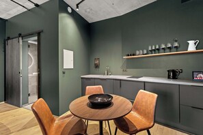 Eine moderne Küche mit einem runden Holztisch und zwei Stühlen, einer Kaffeemaschine sowie einem Regal mit Gläsern und einer Kanne.
