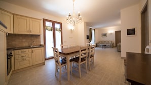 A spacious kitchen with a dining table and chairs, a chandelier, and a sofa in the living area.