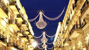 Una concurrida calle urbana nocturna con candelabros ornamentales colgando sobre ella.