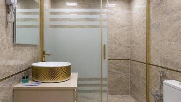 Un bany amb dutxa de vidre, vàter i un lavabo amb una banya amb disseny daurat.