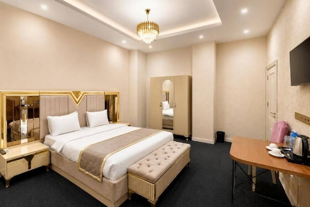 A hotel room with a large bed, bedside tables, a desk, a television, and a wardrobe.