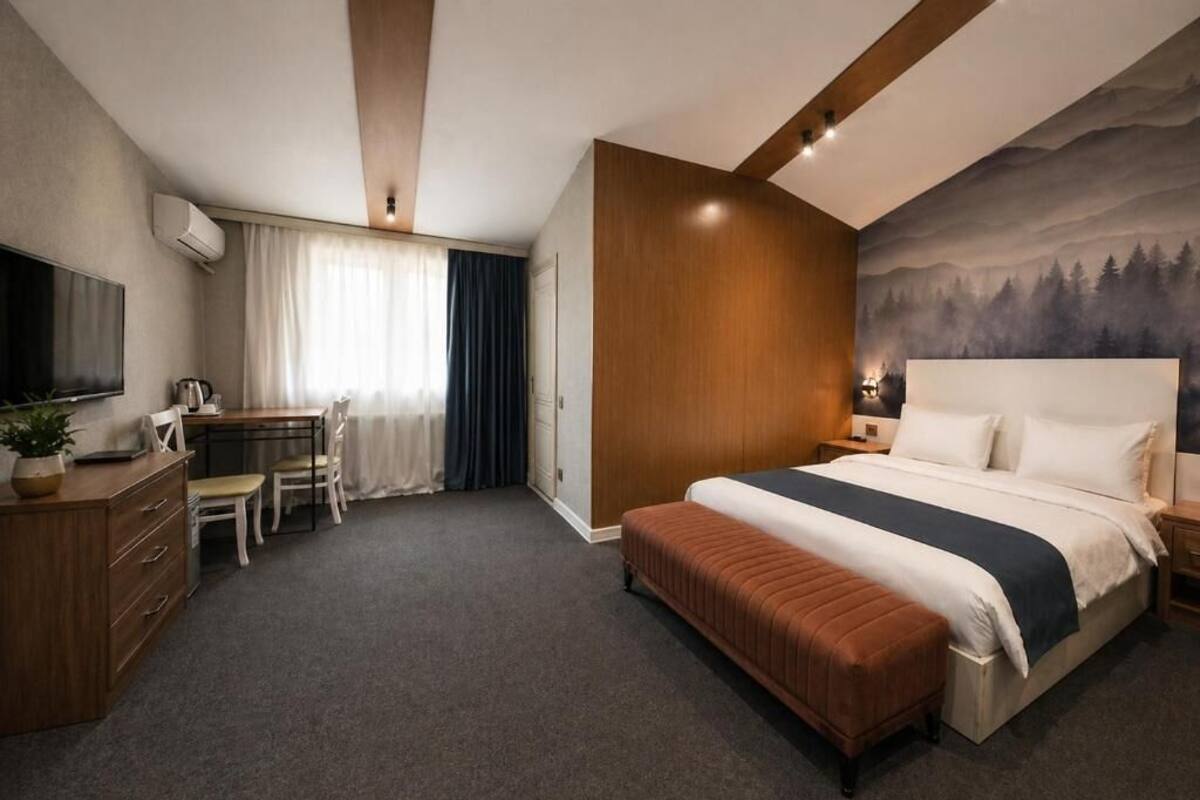 A hotel room with a bed, a desk, a chair, a television, and a painting on the wall.