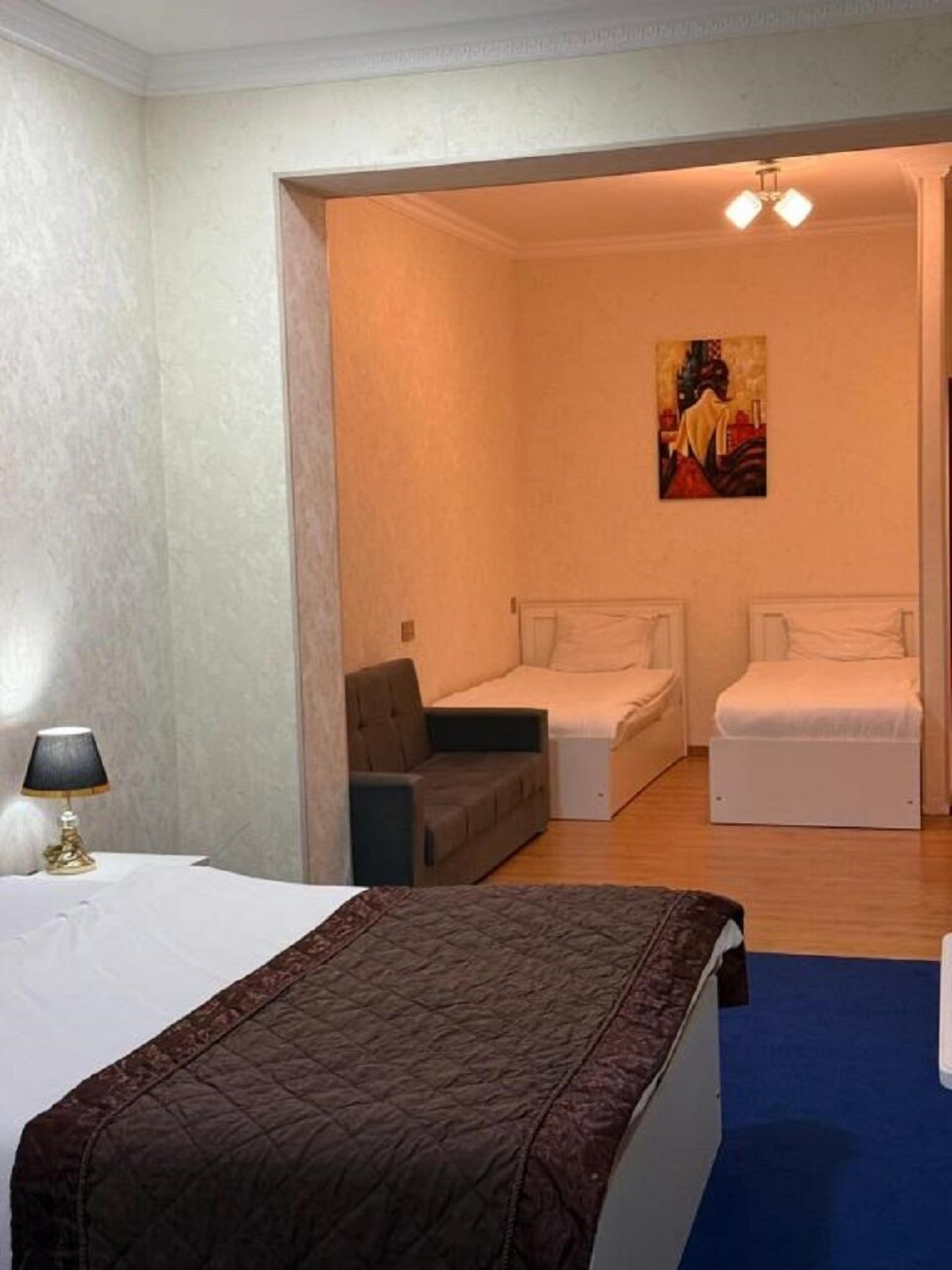 A hotel room with a bed, two bedside tables, a sofa, and a painting on the wall.