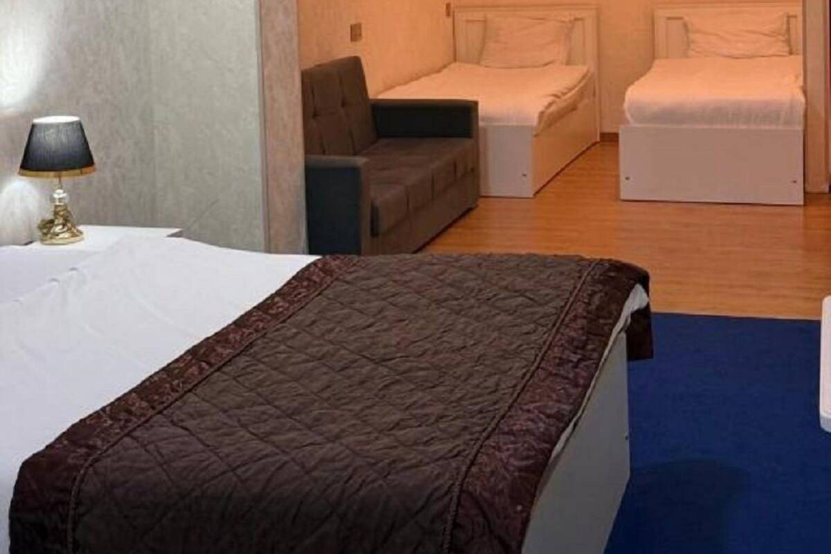 A hotel room with a bed, two bedside tables, a sofa, and a painting on the wall.