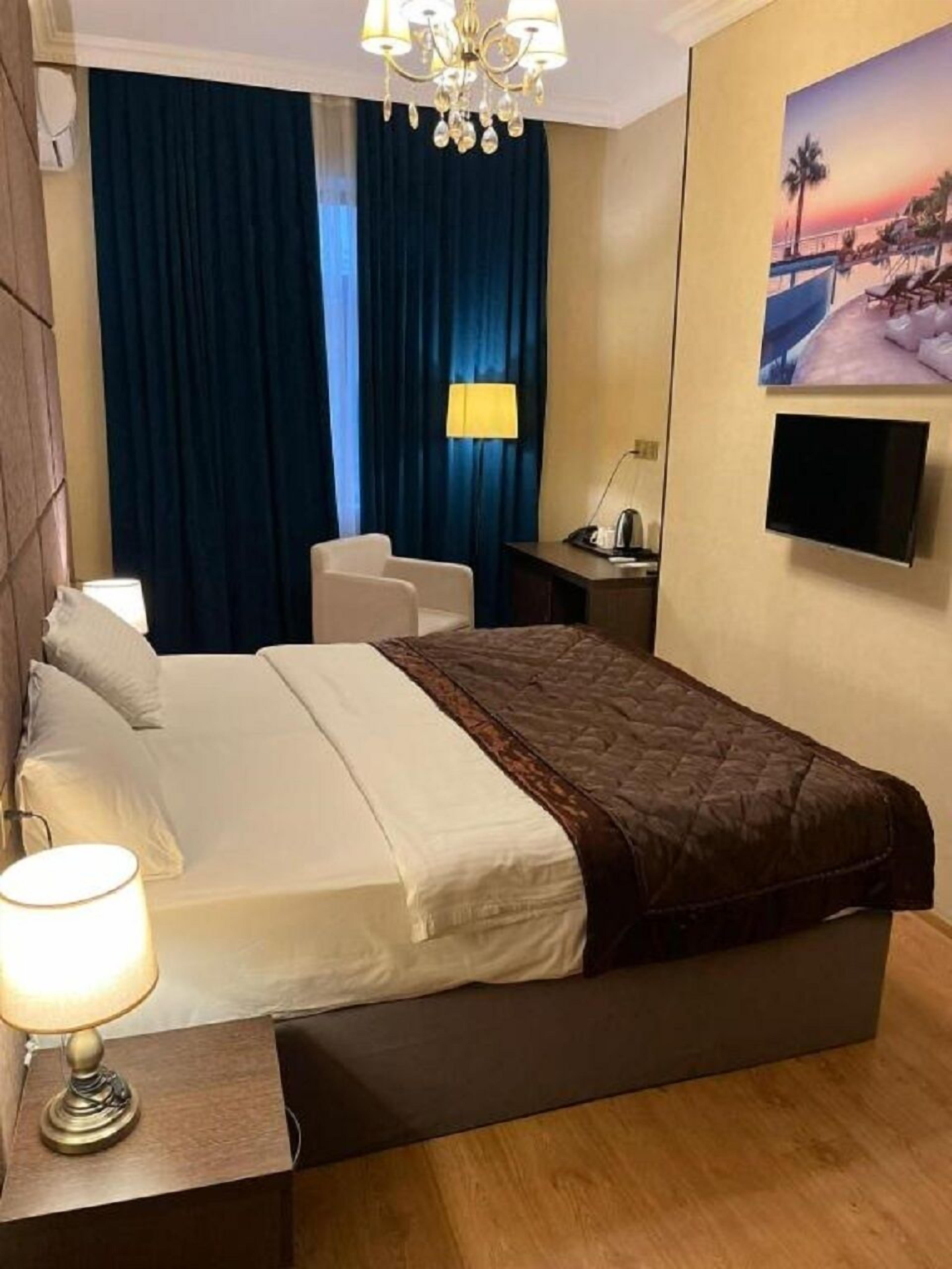 A hotel room with a bed, bedside table, lamp, chair, curtains, and a TV mounted on the wall.