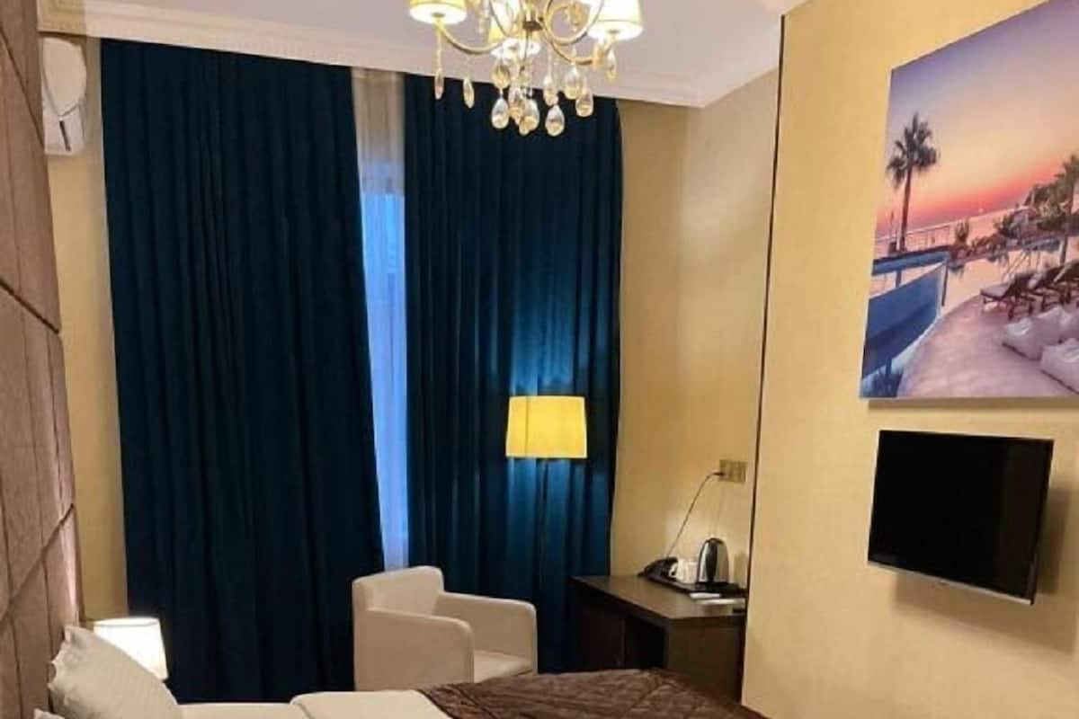 A hotel room with a bed, bedside table, lamp, chair, curtains, and a TV mounted on the wall.