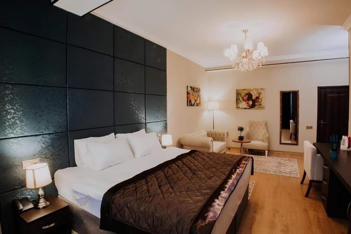 Un dormitorio con una cama grande, una mesita de noche con lámpara, una silla, un escritorio y una araña.