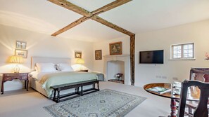 A bedroom with a bed, bedside tables, a bench, a fireplace, a television, and a dining table with chairs.