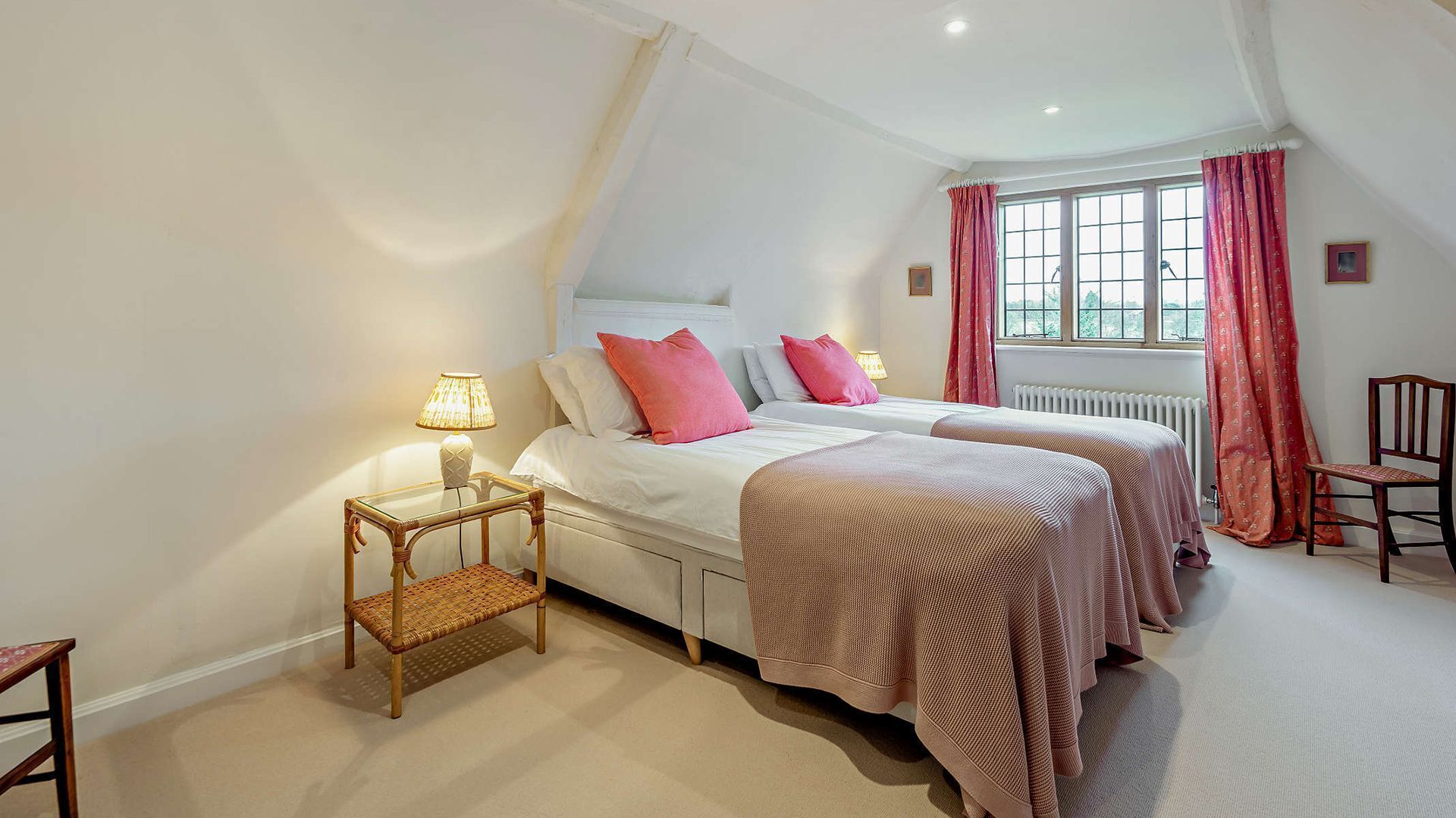 A bedroom with two beds, a nightstand, a chair, and a window with curtains.