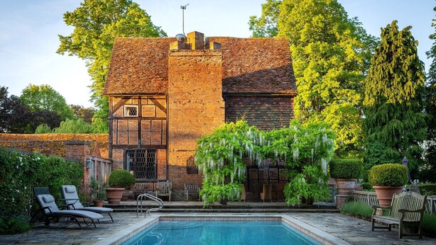 A traditional brick building with a swimming pool, surrounded by lush greenery and outdoor seating. - Chalford Manor - Swimming pool, tennis court, near pub (Oxford)