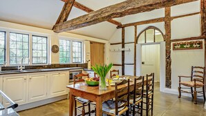 A kitchen with white cabinets, a wooden dining table with chairs, and a large window with multiple panes. - Chalford Manor - Swimming pool, tennis court, near pub (Oxford)