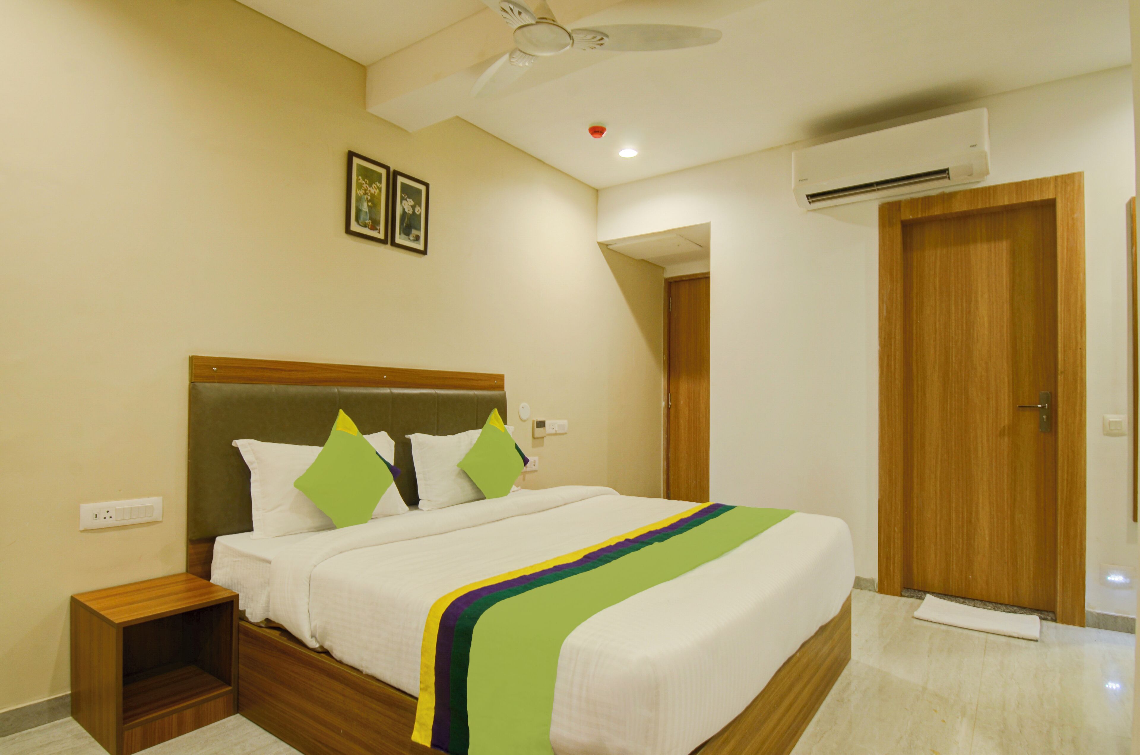 A neatly made bed with a wooden headboard, a bedside table, and a wall-mounted air conditioner.