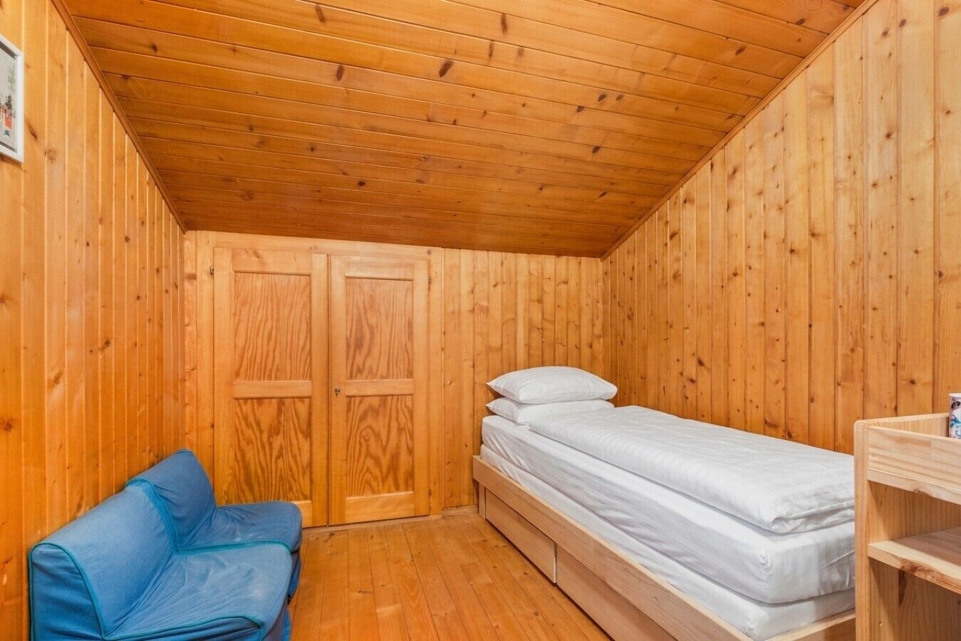 A small, wooden room with a bunk bed, a blue sofa, and a wooden wardrobe.