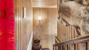 Un intérieur en bois avec un escalier, un luminaire fixé au mur et un objet recouvert de fourrure.