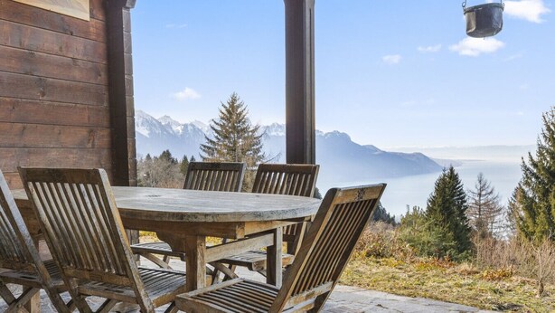 Une table et des chaises en bois sont disposées à l’extérieur, offrant une vue sur la montagne.