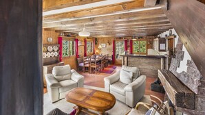 L’intérieur d’un chalet rustique comprend un coin repas, deux canapés, une table basse en bois et une cheminée en pierre.