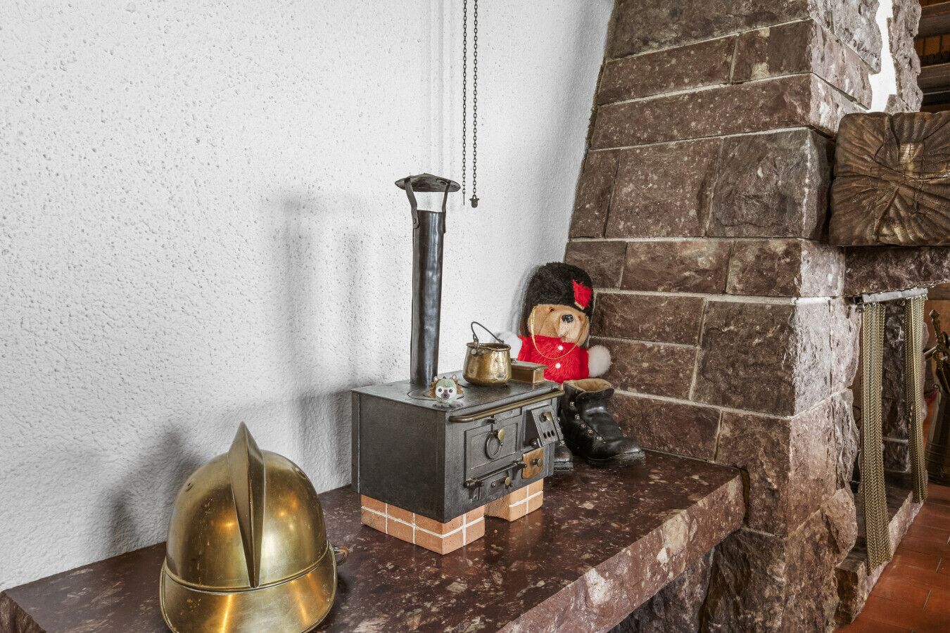 Ein rustikales Interieur mit Kamin aus Stein, einem alten Herd, einem Teddybären und einer Messingglocke.
