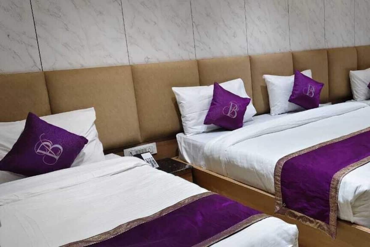 A hotel room with three beds, each with white bedding and purple accents.