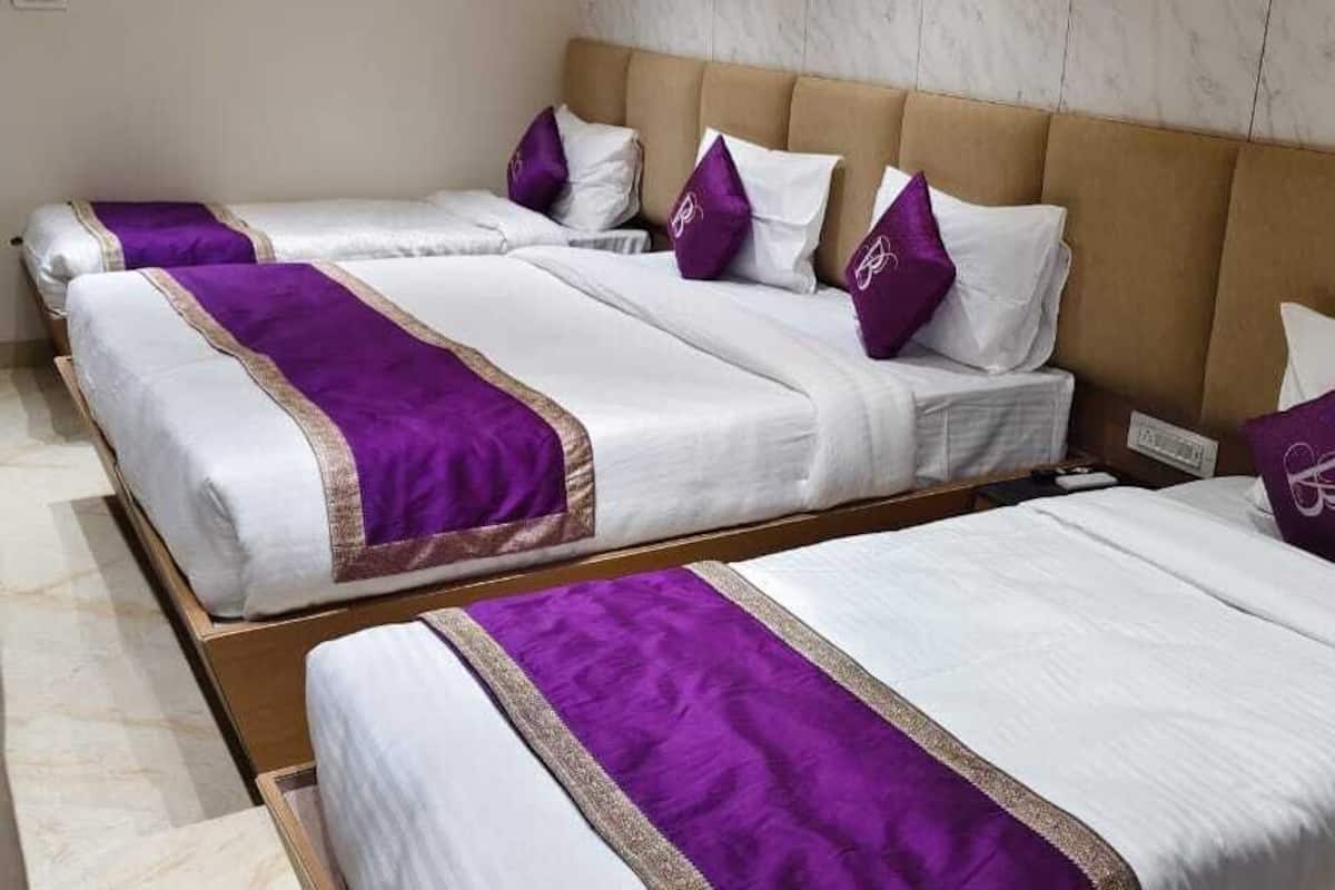 A hotel room with two beds, each with white bedding and purple accents, and a headboard with a logo.