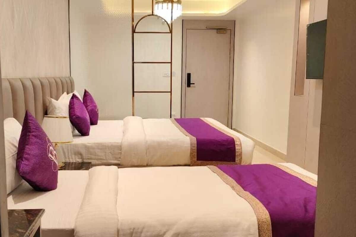 A hotel room with two beds, each with a purple throw blanket and pillows, a wooden ladder, and a door in the background.
