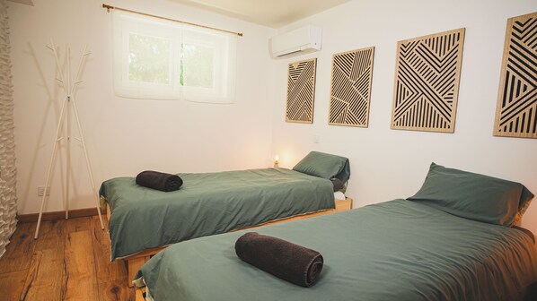 A room with two beds, a window, an air conditioner, and decorative wall panels.