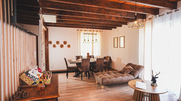 Un comedor con mesa y sillas de madera, un sofá y una lámpara de araña.