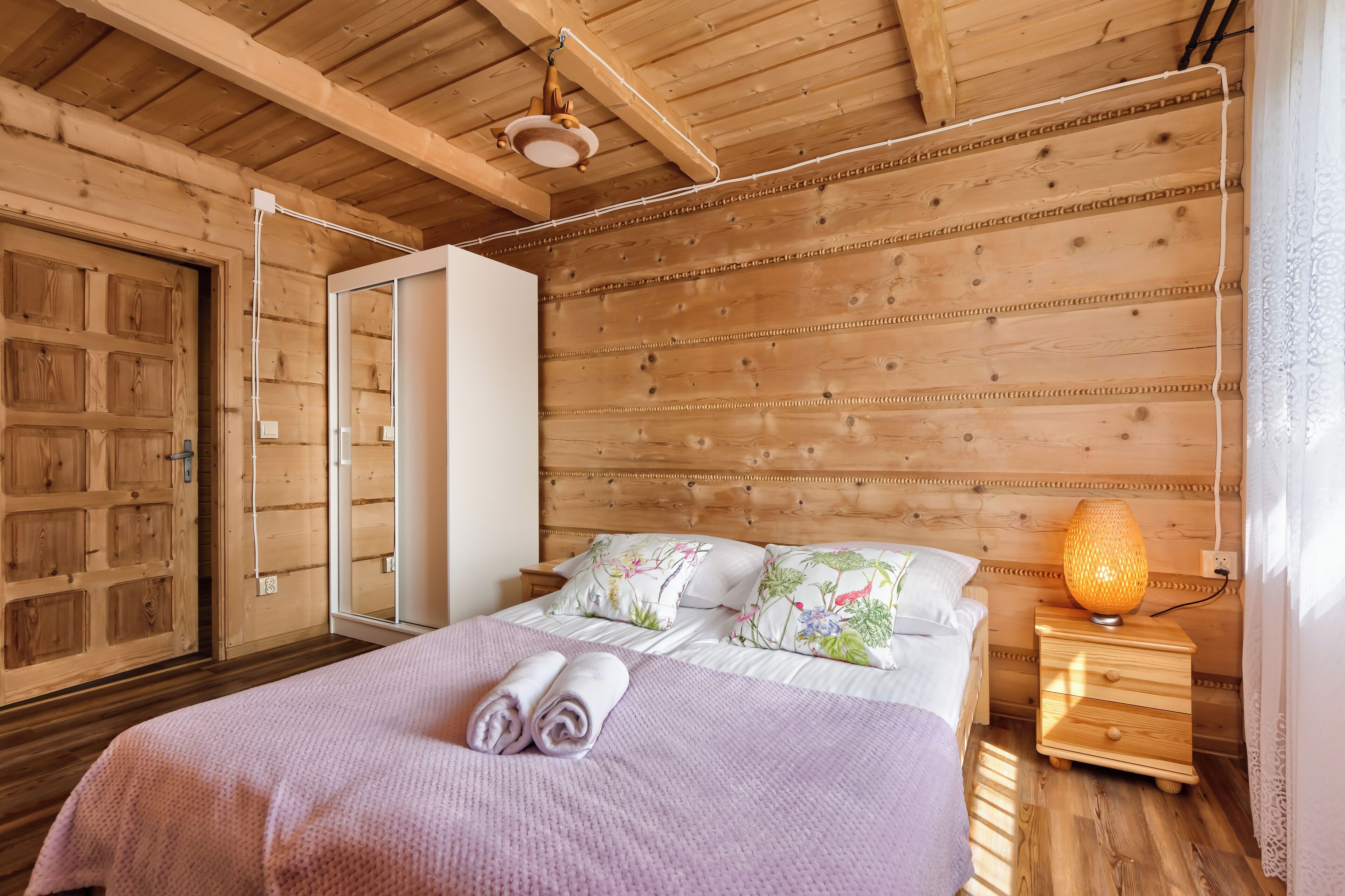 A wooden cabin bedroom with a bed, pillows, a nightstand, and a lamp.