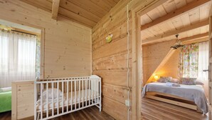 Une chambre dans une cabane en bois, avec un berceau, un lit et un canapé vert.
