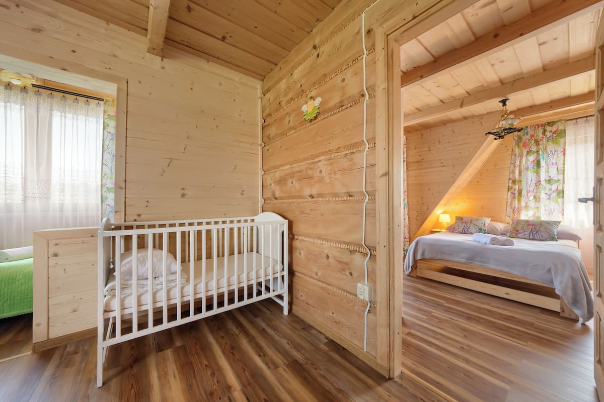 Un dormitorio de cabaña de madera con una cuna, una cama y un sofá verde.